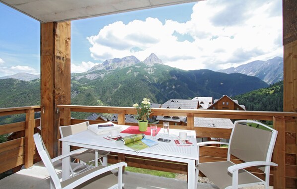 A wooden deck with a table and chairs, overlooking a mountainous landscape with houses.