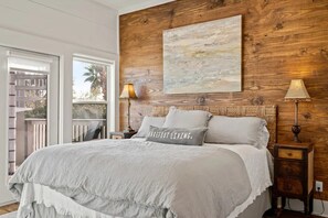 A bedroom with a large bed, a wooden headboard, two bedside tables with lamps, and a view through a glass door.