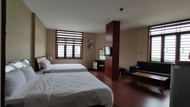 Een hotelkamer met twee bedden, een bureau, een stoel, een bank en grote ramen met zonwering.