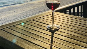 Ein Glas Rotwein auf einer Holzterrasse mit Blick auf einen Strand, das Meer und einen untergehenden Sonnenuntergang.