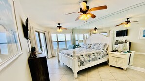 Ein Schlafzimmer mit einem Bett, einem Nachttisch, einer Kommode, einem Deckenventilator und einem großen Fenster.