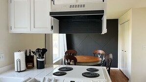 Una cocina con armarios blancos, estufa y una mesa de comedor con sillas.