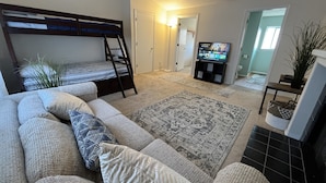 Una sala de estar con una cama litera, un sofá, un televisor y una alfombra.