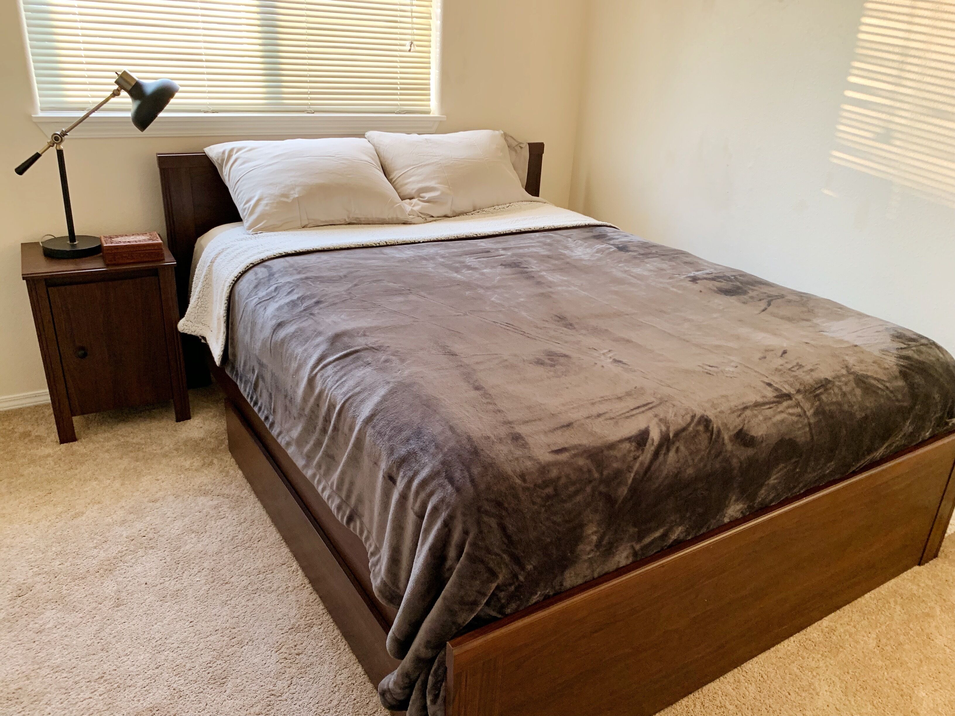 A bedroom with a bed, a nightstand, a lamp, and a window with blinds.