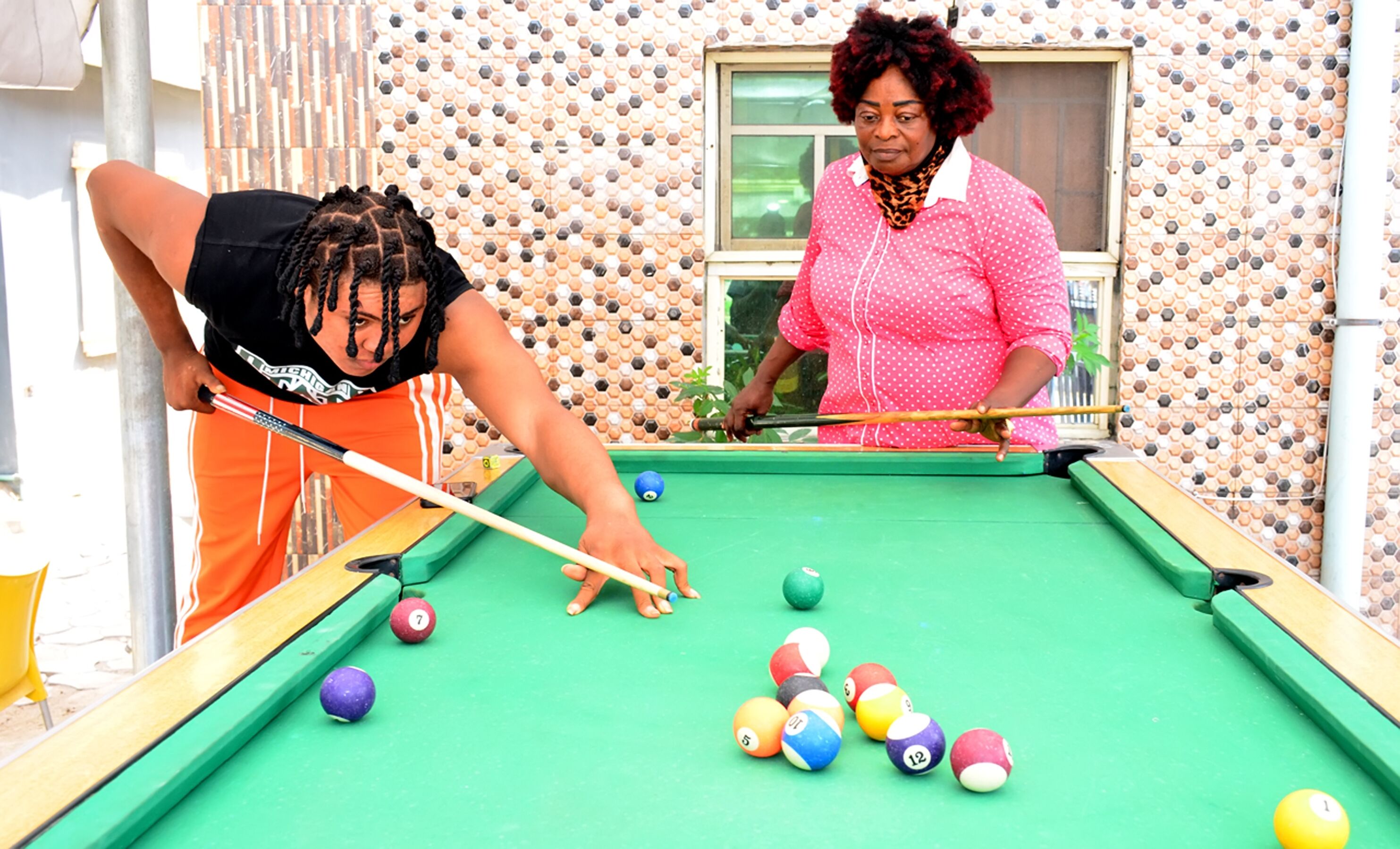 Two individuals playing pool with a green table and colorful balls.