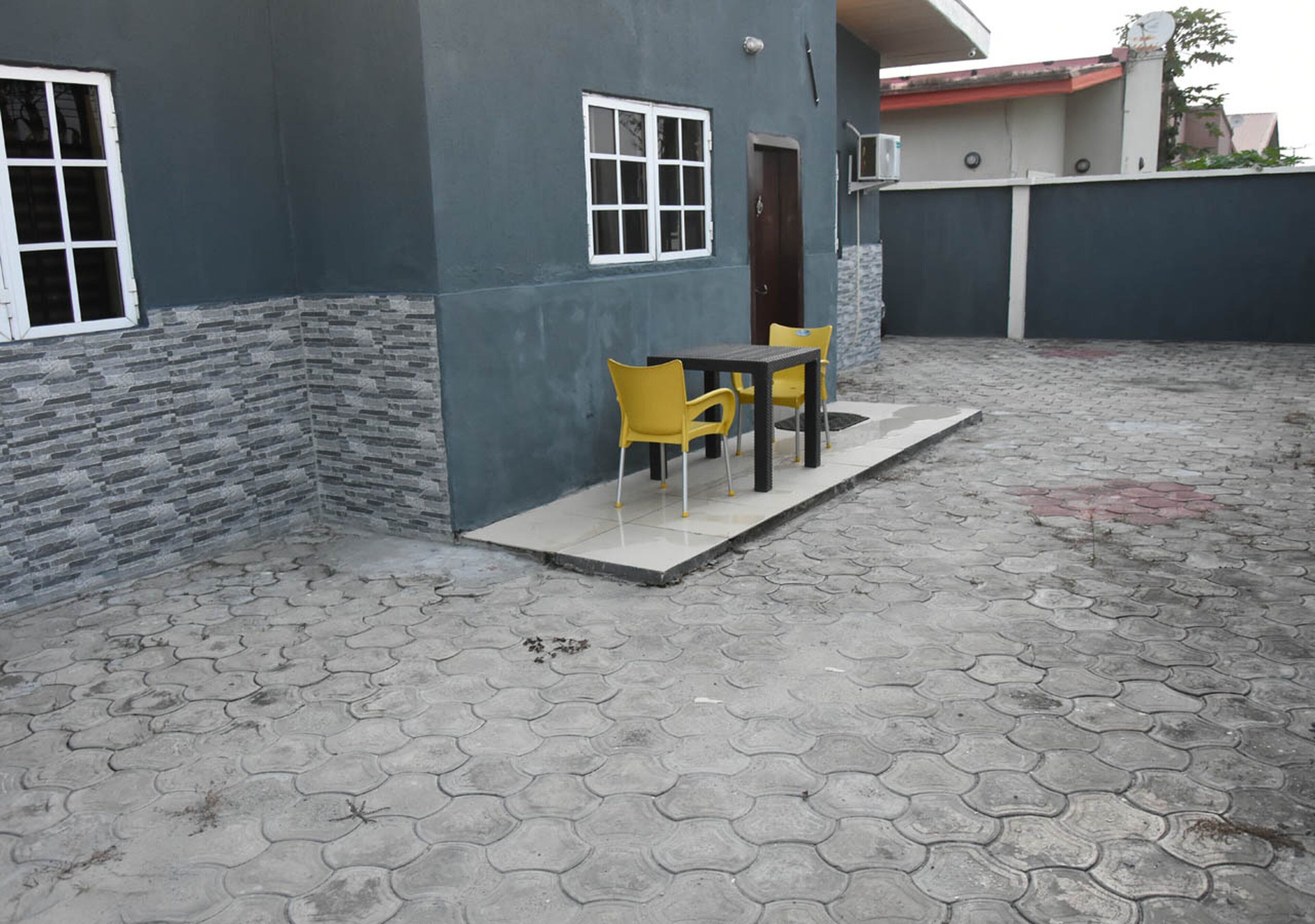 A building with a grey exterior, a stone accent wall, a door, and a small patio area with a table and two chairs.
