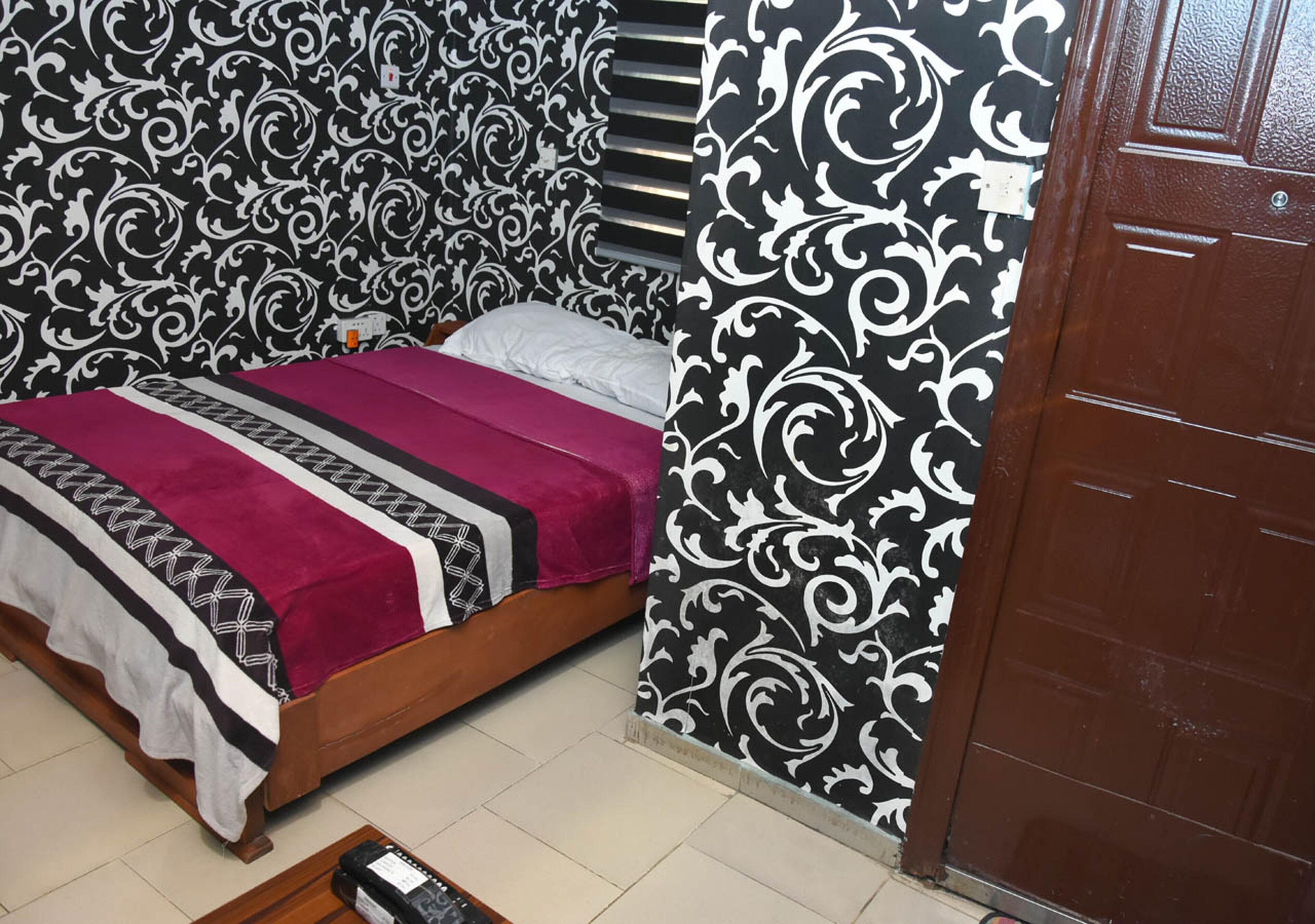 Un dormitorio con cama, armario de madera y papel tapiz estampado.