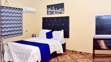 Habitación de hotel con una cama, aire acondicionado de pared, un cuadro de paisaje urbano y un televisor.
