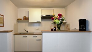 Een praktische keuken met witte kastjes, een roestvrijstalen afzuigkap, een spoelbak en een koffiezetapparaat.