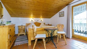 A cozy room with a wooden ceiling, a bed with pillows, a small table, a chair, a dresser, and a window with curtains. - Cozy apartment, 45m², balcony and separate kitchen (Reit im Winkl)