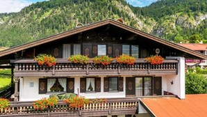 A traditional chalet with a balcony adorned with flowers, set against a mountainous backdrop. - Cozy apartment, 45m², balcony and separate kitchen (Reit im Winkl)