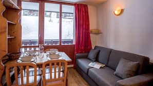 A cozy room with a dining table set for four, a grey sofa, and a window with a view of a snowy landscape. - Rond Point des Pistes (Val Claret) by Interhome (Tignes)