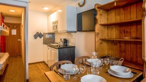 A compact kitchen with a microwave, stove, and sink. There is a dining table set with plates, glasses, and a basket. - Rond Point des Pistes (Val Claret) by Interhome (Tignes)