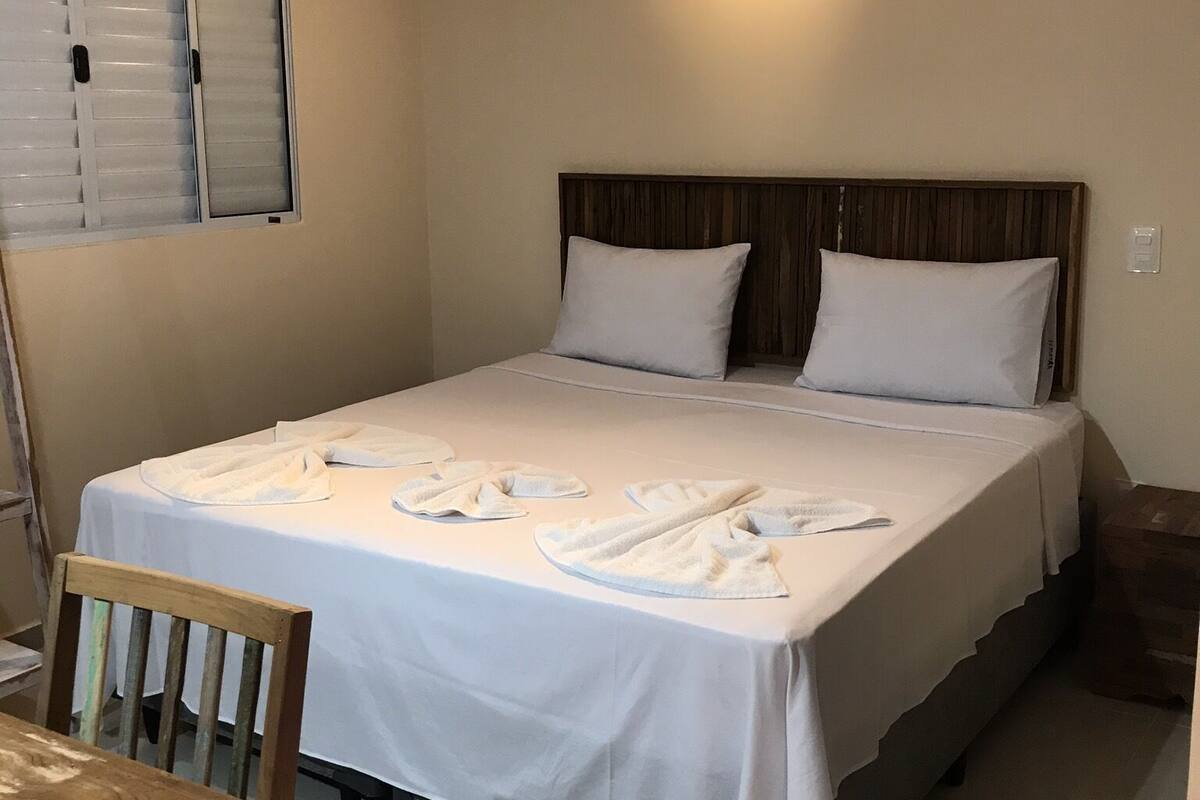 Ein ordentlich bezogenes Bett mit weißen Leinen und Handtüchern, ein hölzerner Kopfseitenverkleidung und einer Deckenleuchte.