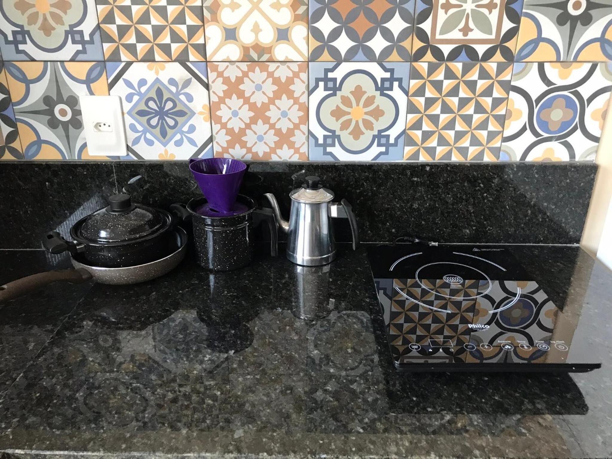 Una cocina con encimera negra, estufa, olla, hervidor y colador morado.