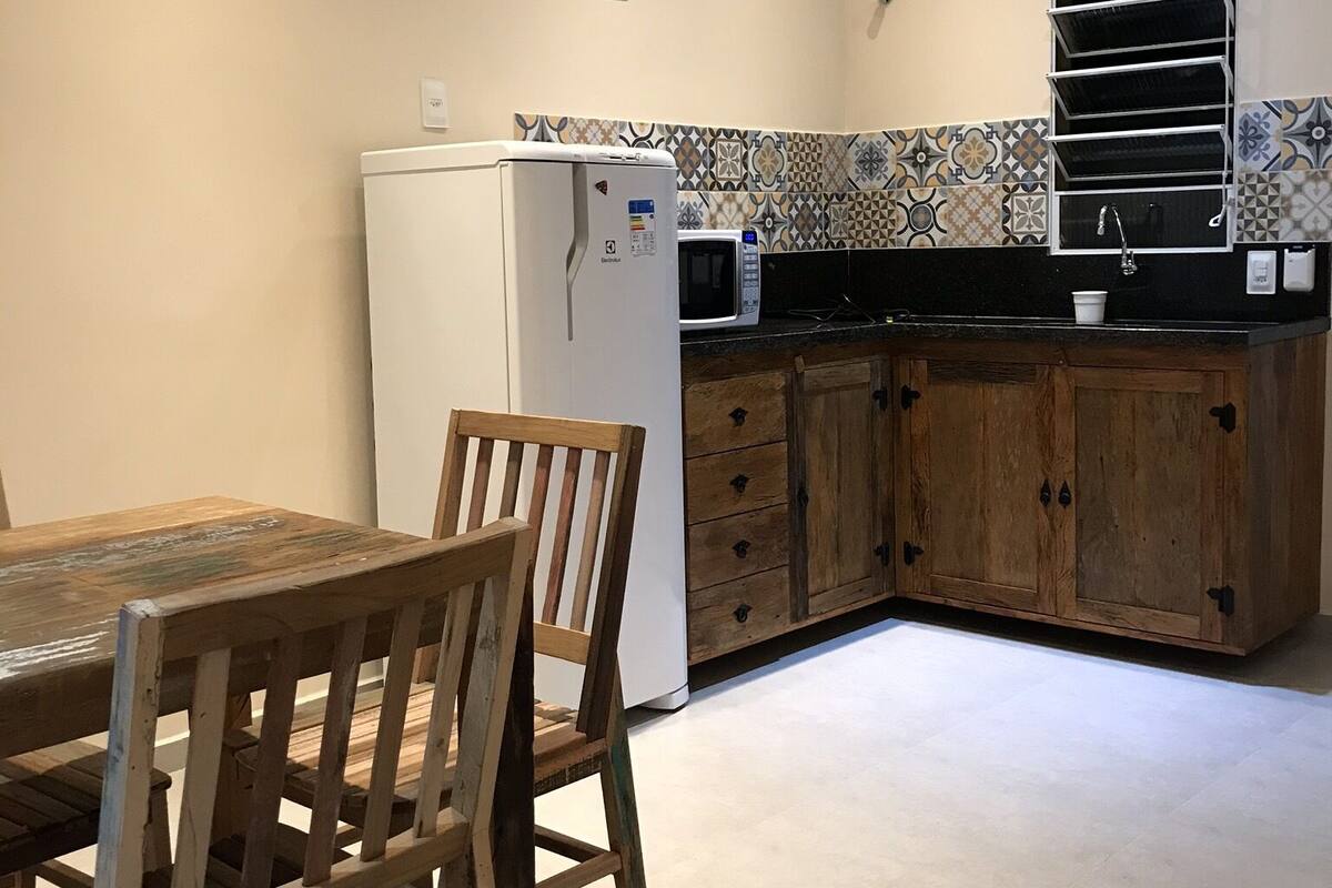 Eine kompakte Küche mit Kühlschrank, Mikrowelle und Spüle. Ein Holztisch mit Stühlen und eine geflieste Spritzschutzwand sind vorhanden.