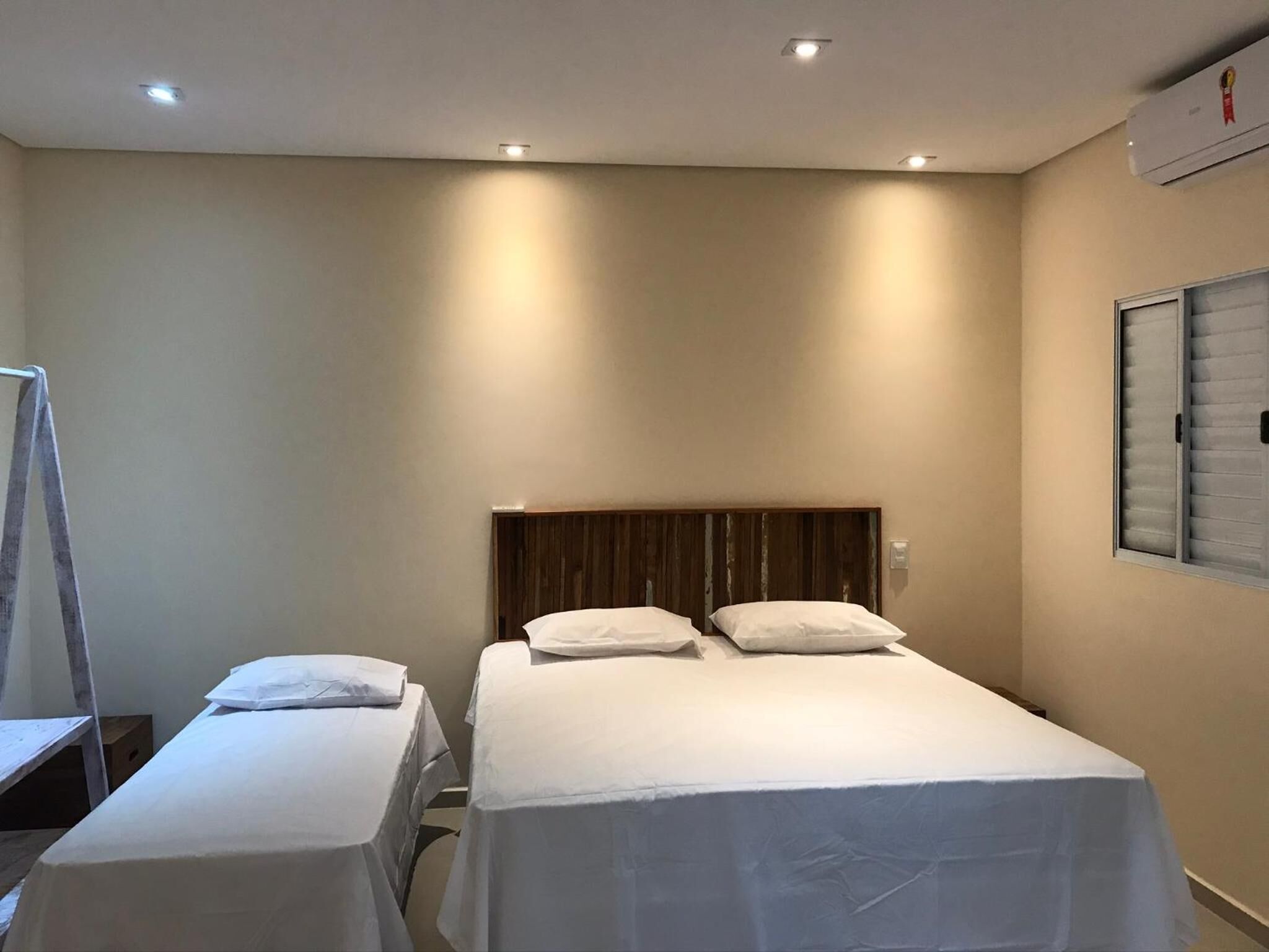 Una habitación con dos camas individuales, un cabecero de madera y una ventana con persianas.