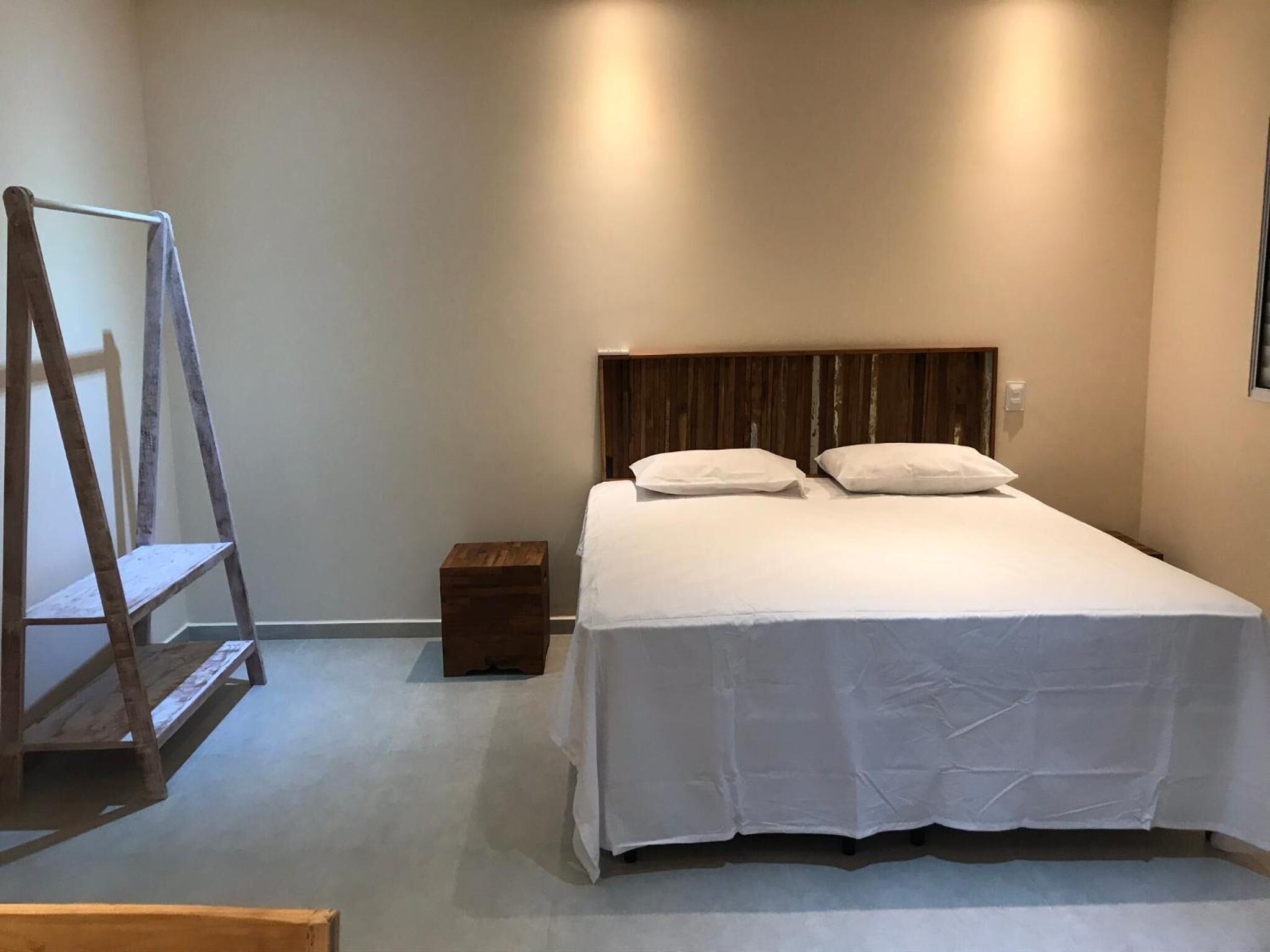 A neatly arranged bedroom with a bed, a small wooden nightstand, and a wooden ladder.