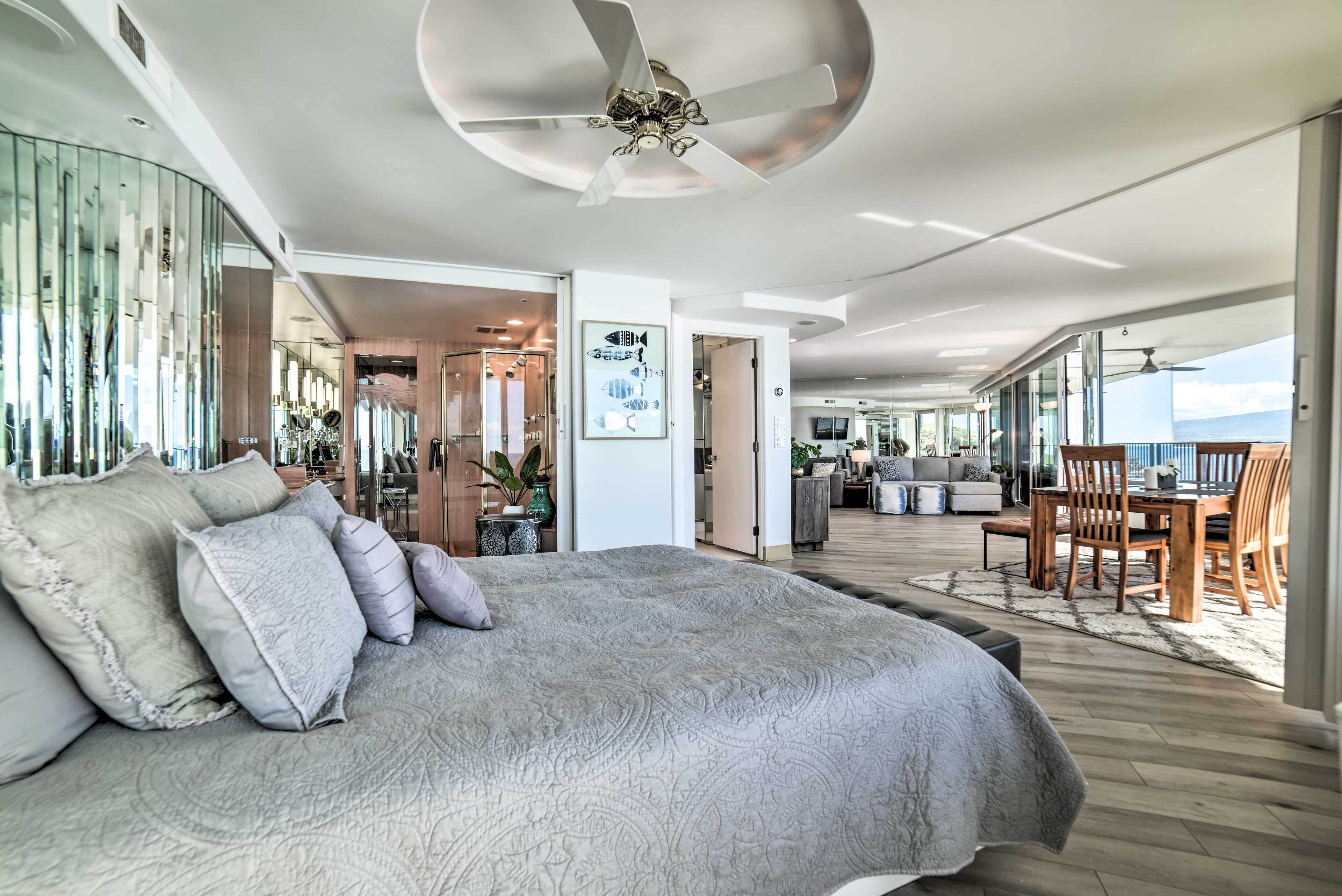 Une chambre spacieuse avec un grand lit, un ventilateur de plafond et une vue sur le salon.