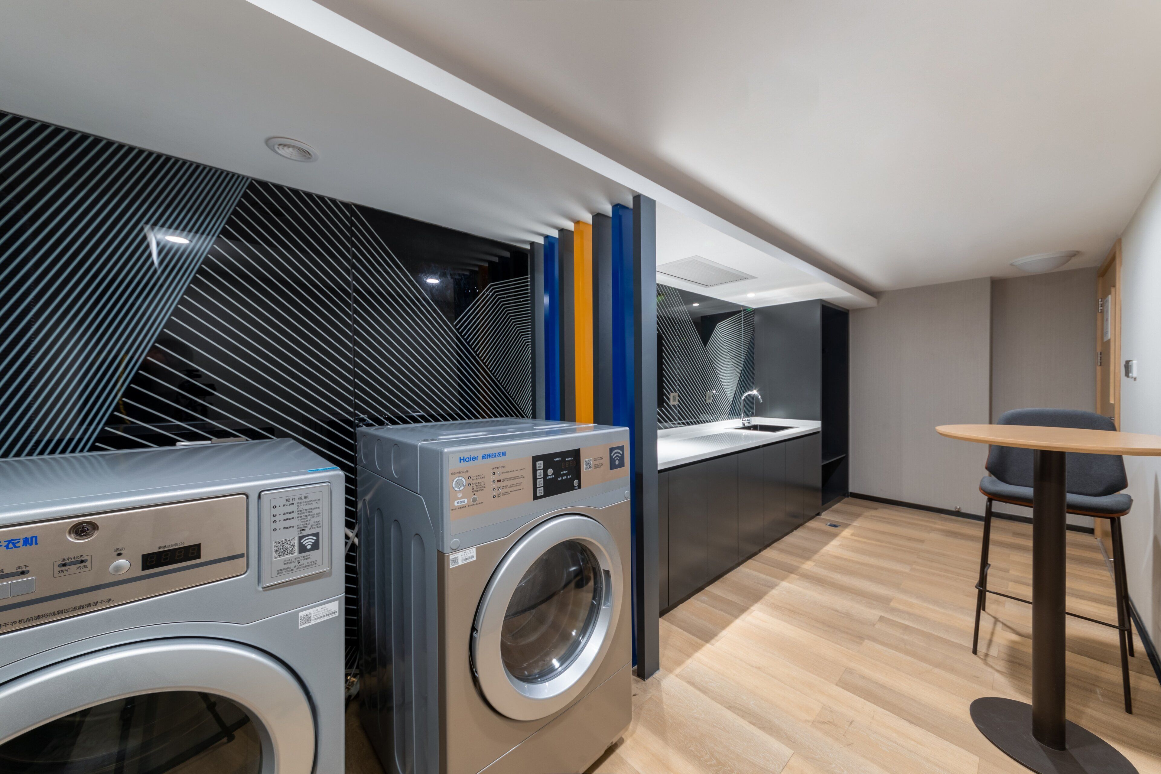 A modern laundry room with stacked washers and dryers, a sink, and a small table with chairs.