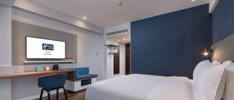 Une chambre d’hôtel moderne avec un lit, un bureau et une chaise, une télévision et un mur bleu.