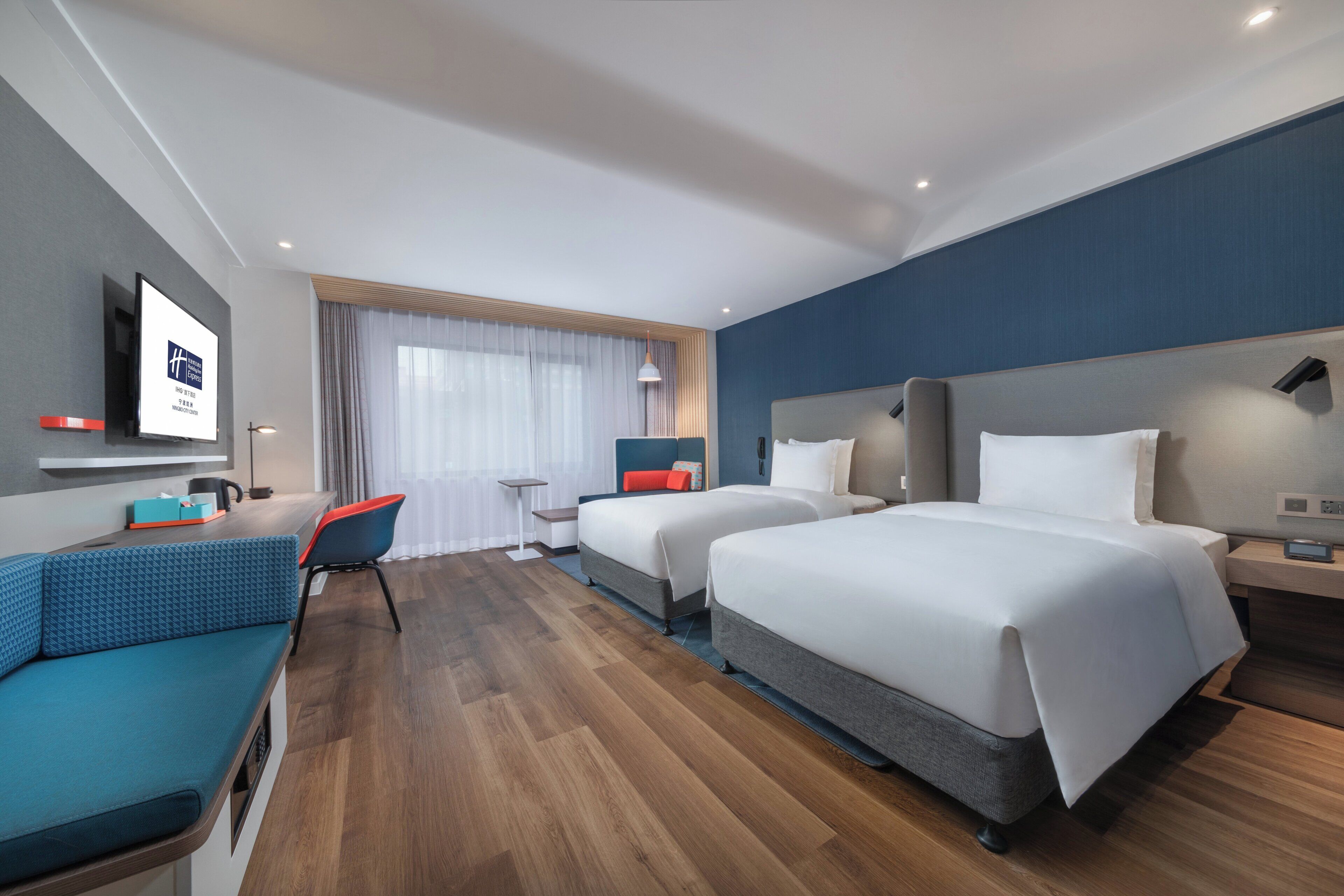 Habitación de hotel con dos camas, un escritorio, una silla y un televisor.