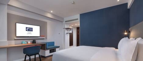 A modern hotel room with a bed, desk, chair, and a television displaying a sign.