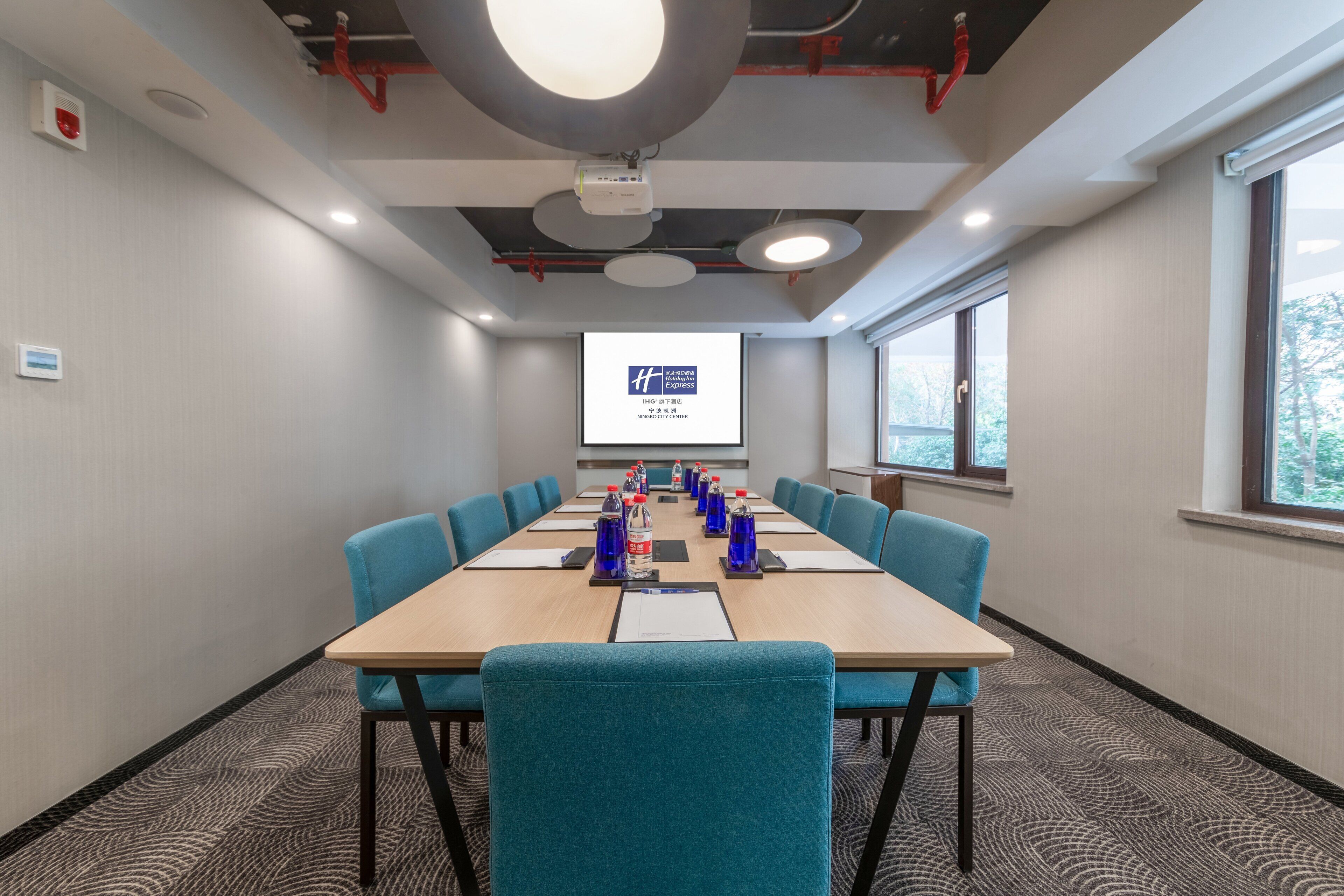 A conference room with a long table, blue chairs, and a projector screen displaying a presentation.