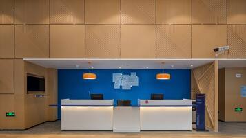 A reception desk with a blue wall and wooden paneling above. There are two receptionists behind the desk, and a sign above them.