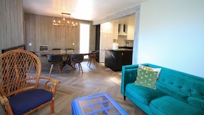 A modern living room with a teal sofa, a wicker chair, a dining table with chairs, and a kitchen area in the background. - Mammoth Ski & Racquet Club #51 - Pet Friendly (Mammoth Lakes)