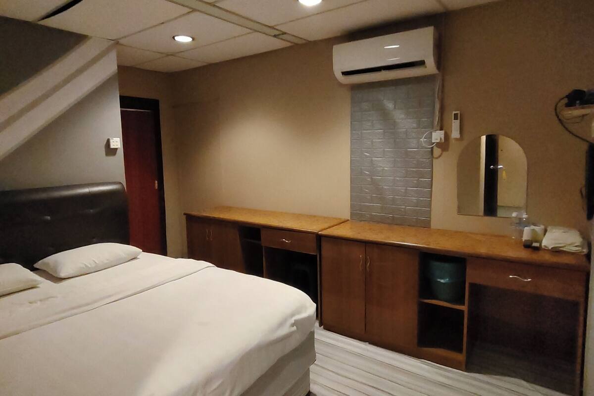 Een hotelkamer met een bed, een houten bureau, een spiegel en een airconditioning.