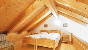 Ein gemütliches Schlafzimmer im Dachgeschoss mit holzgetäfelter Schräge, einem Doppelbett, einem kleinen Nachttisch und einer gestreiften Couch.
