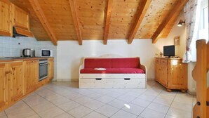 Ein gemütliches Zimmer mit Holzbalkendecke, einem roten Sofa, einem Fernseher und einer Küchenzeile mit Holzausstattung und einer Mikrowelle.