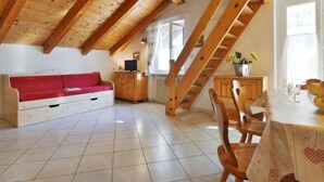 Ein gemütliches Dachzimmer mit einem roten Sofa, einem Holzesstisch und einer Treppe.