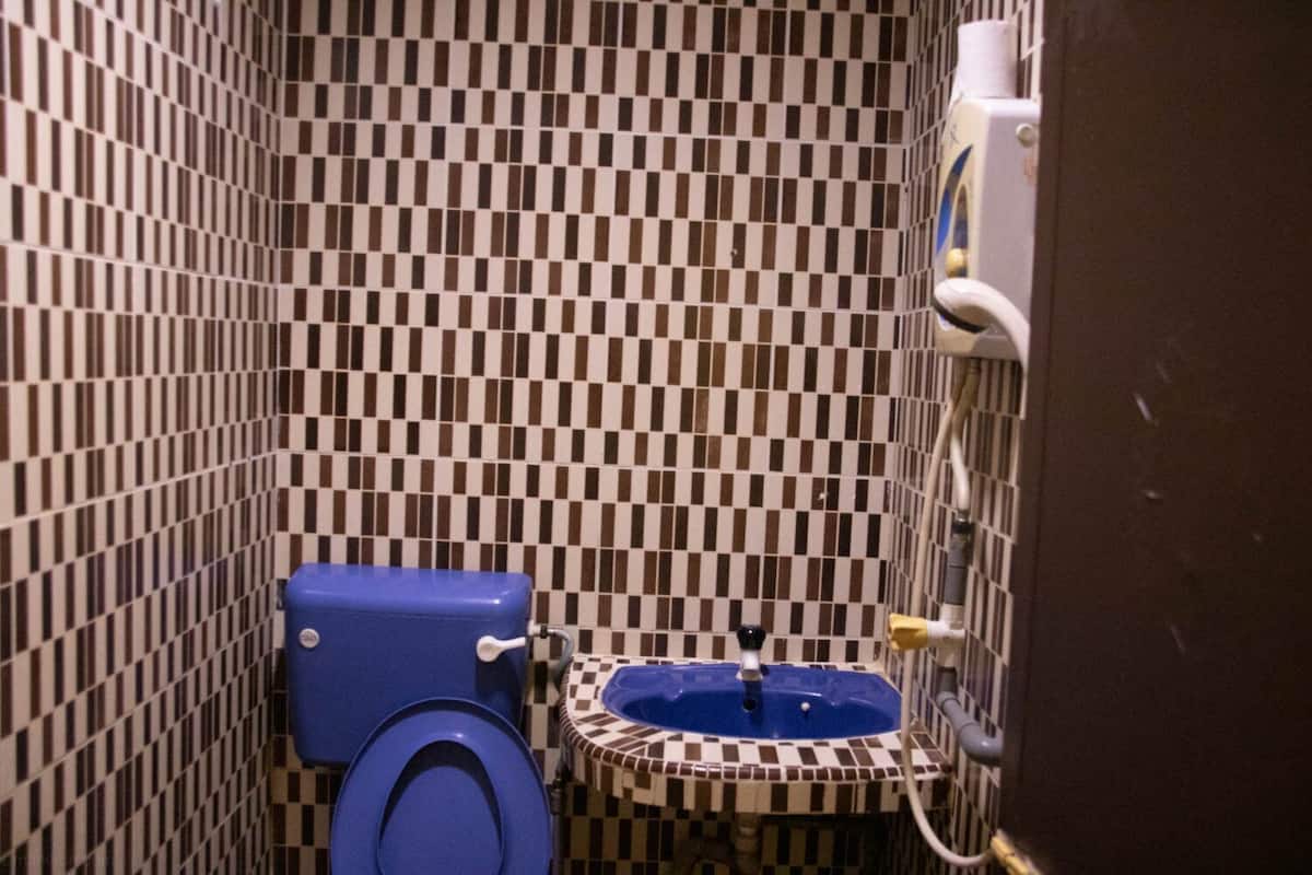 Et badeværelse med væg af skakmønstrede fliser, et blåt toilet og en lille vask med en base af skakmønstrede fliser.