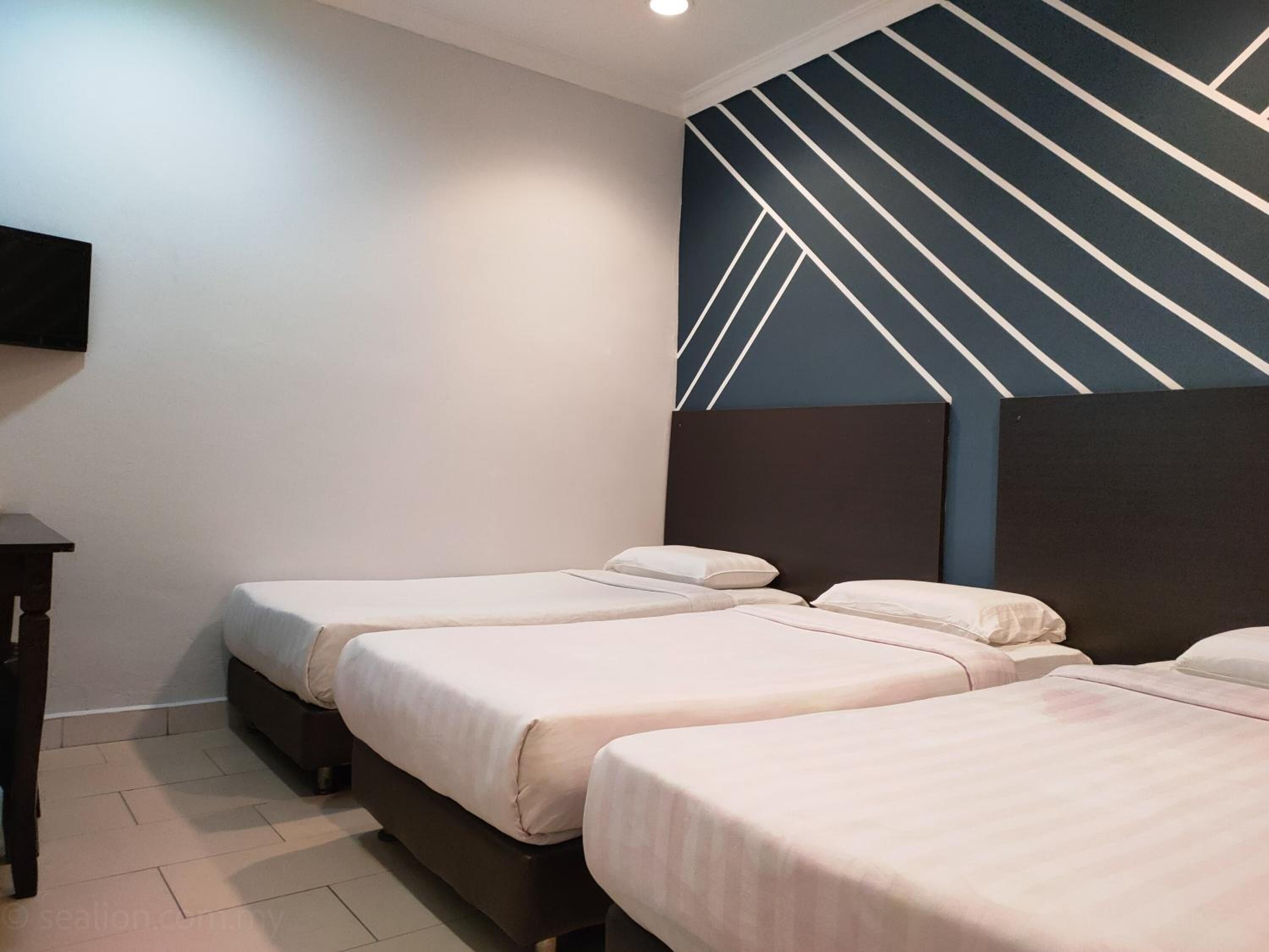 A hotel room with three single beds, a dark headboard, a flat-screen TV mounted on the wall, and a tiled floor.