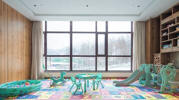 A children's playroom with a large window, colorful play mat, and various toys.