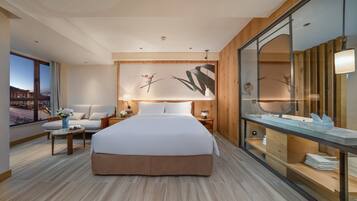 A modern hotel room with a large bed, a seating area with a table, a large window with a view, and a wooden accent wall.