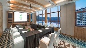 A conference room with a large screen displaying text, a long table with chairs, and large windows offering a view of a building and a snowy landscape. - Holiday Inn Jilin Beidahu by IHG (Jilin)
