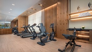 A gym with multiple treadmills and exercise bikes, wooden walls, and a large window. - Holiday Inn Jilin Beidahu by IHG (Jilin)