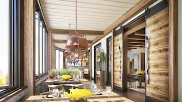A spacious dining area with wooden tables and chairs, a central hanging light fixture, and a view through large windows.