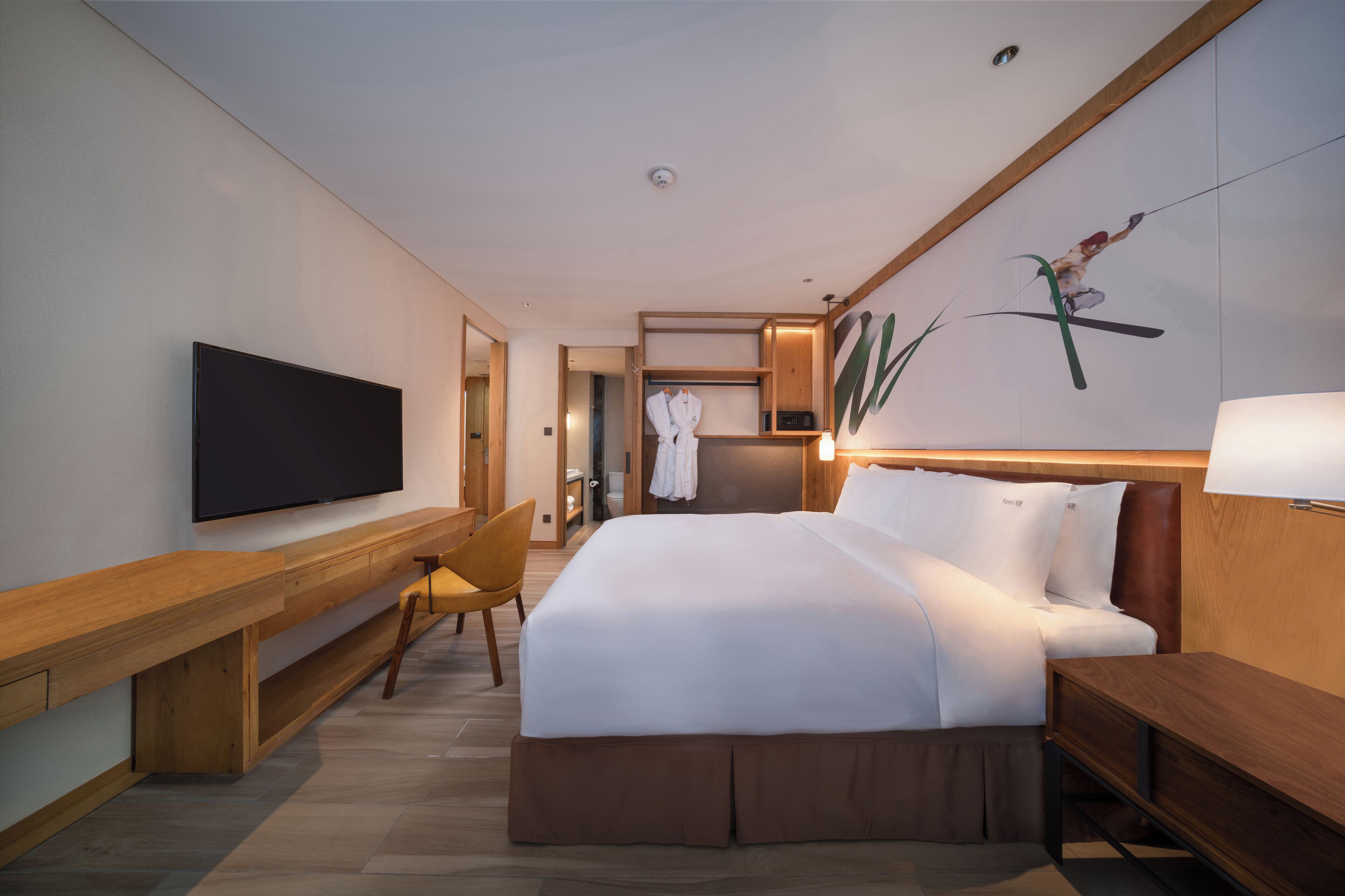 A modern hotel room with a large bed, a TV, a wooden desk, and a chair.