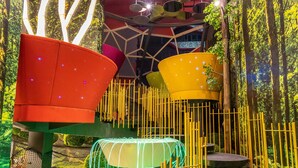 Un jardín interior moderno con diversas opciones de asientos, incluyendo una silla roja y una maceta amarilla.