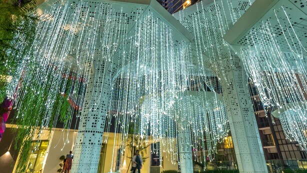 Una plaza urbana moderna con una instalación de luces geométricas, rodeada de rascacielos.