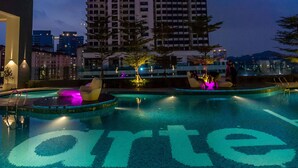 Vista nocturna de un rascacielos con una piscina al frente.