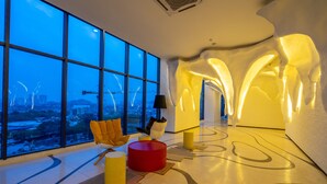 Un interior moderno con ventanas amplias, un reposapiés rojo y vistas a la ciudad.
