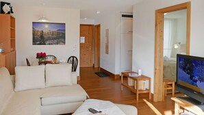 Ein modernes Wohnzimmer mit einer Couch, einem Fernseher und einem Holztisch. An der Wand hängt ein Gemälde und eine Tür führt in einen anderen Raum.