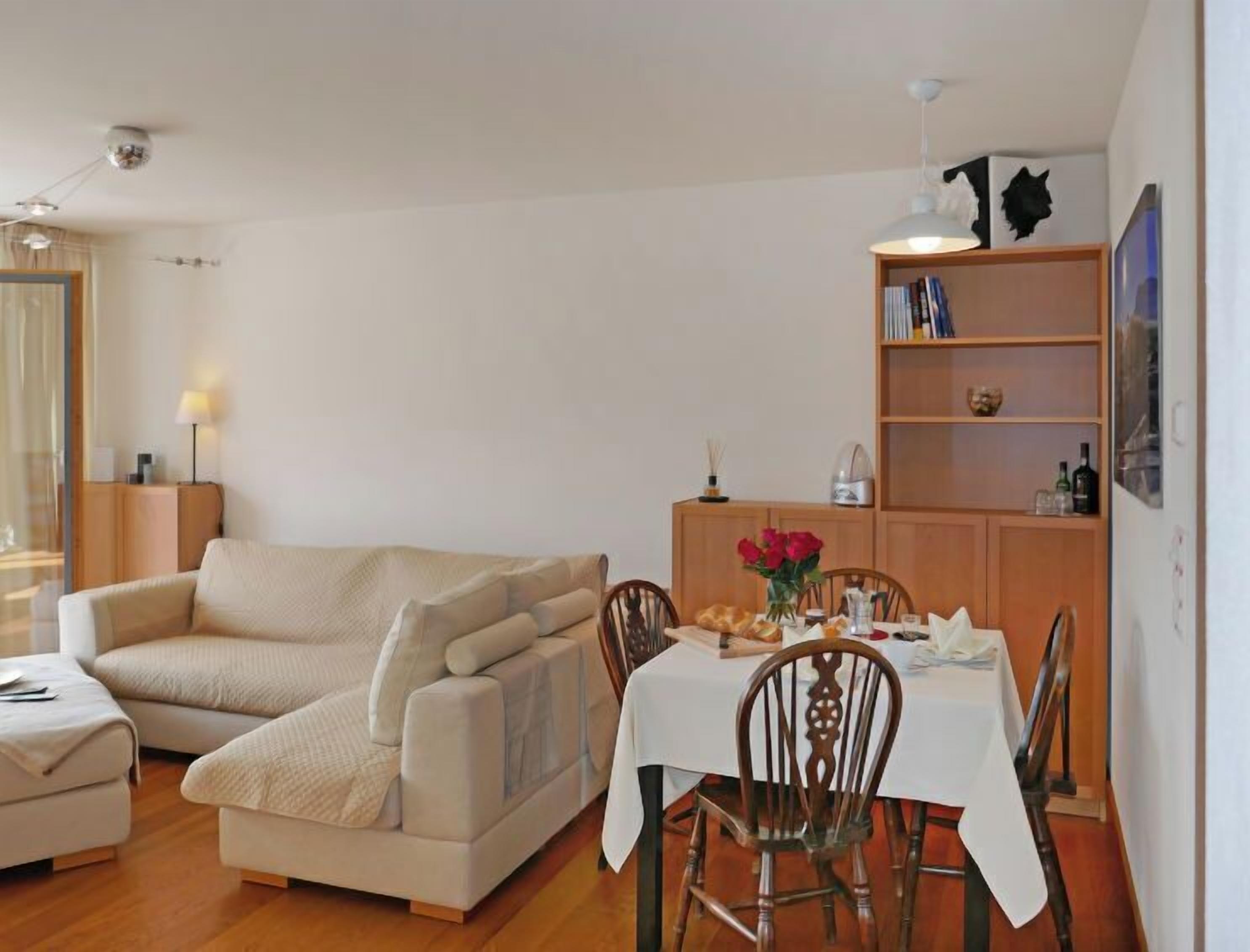 Ein Wohnzimmer mit einer Couch, einem Esstisch mit Stühlen, einem Bücherregal und einer Lampe.
