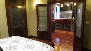 A bedroom with a large bed, a wooden floor, and a view into a kitchen area with a bar. - Modern meets Historic, Natural Lighting + High Ceilings, Near Metro (Belleville)