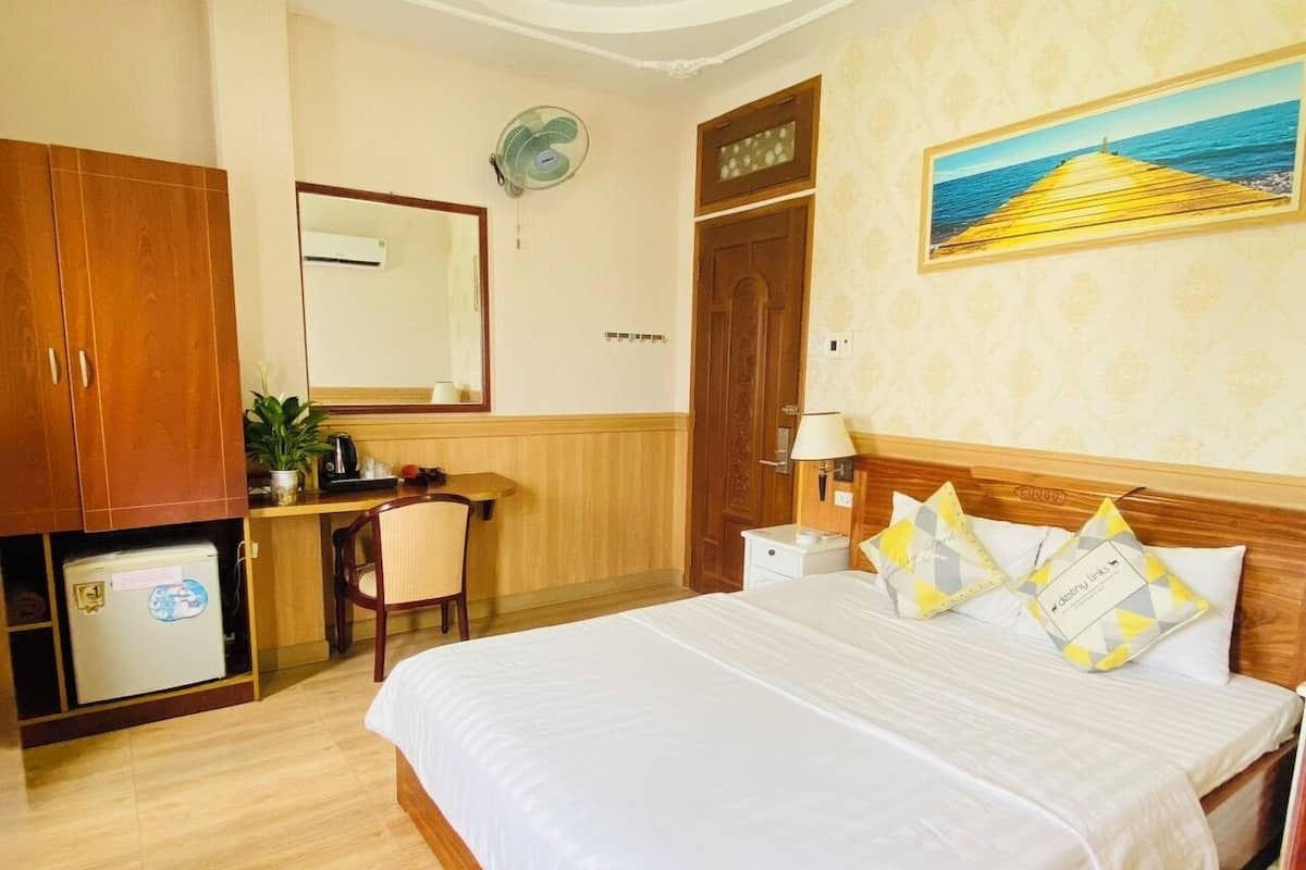 Ein Hotelzimmer mit Bett, Schreibtisch, Stuhl, Kleiderschrank, Spiegel, Wandventilator und einem Bild eines Piers.
